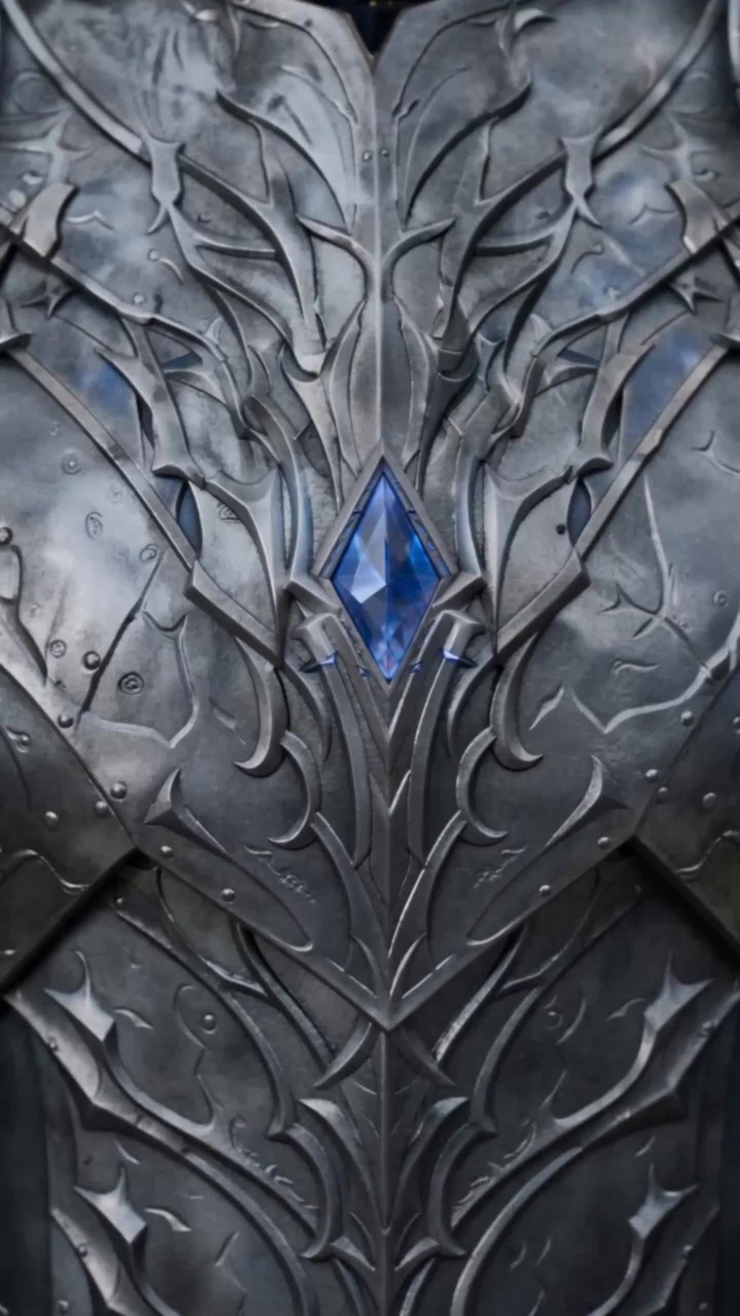 Close-up of silver armor with embossed details and a blue jewel on the chest