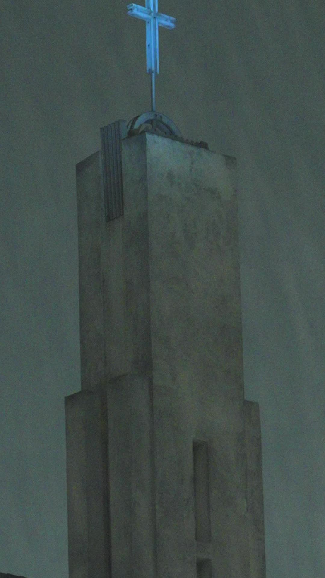 Concrete church bell tower at night with a blue-lit cross on top