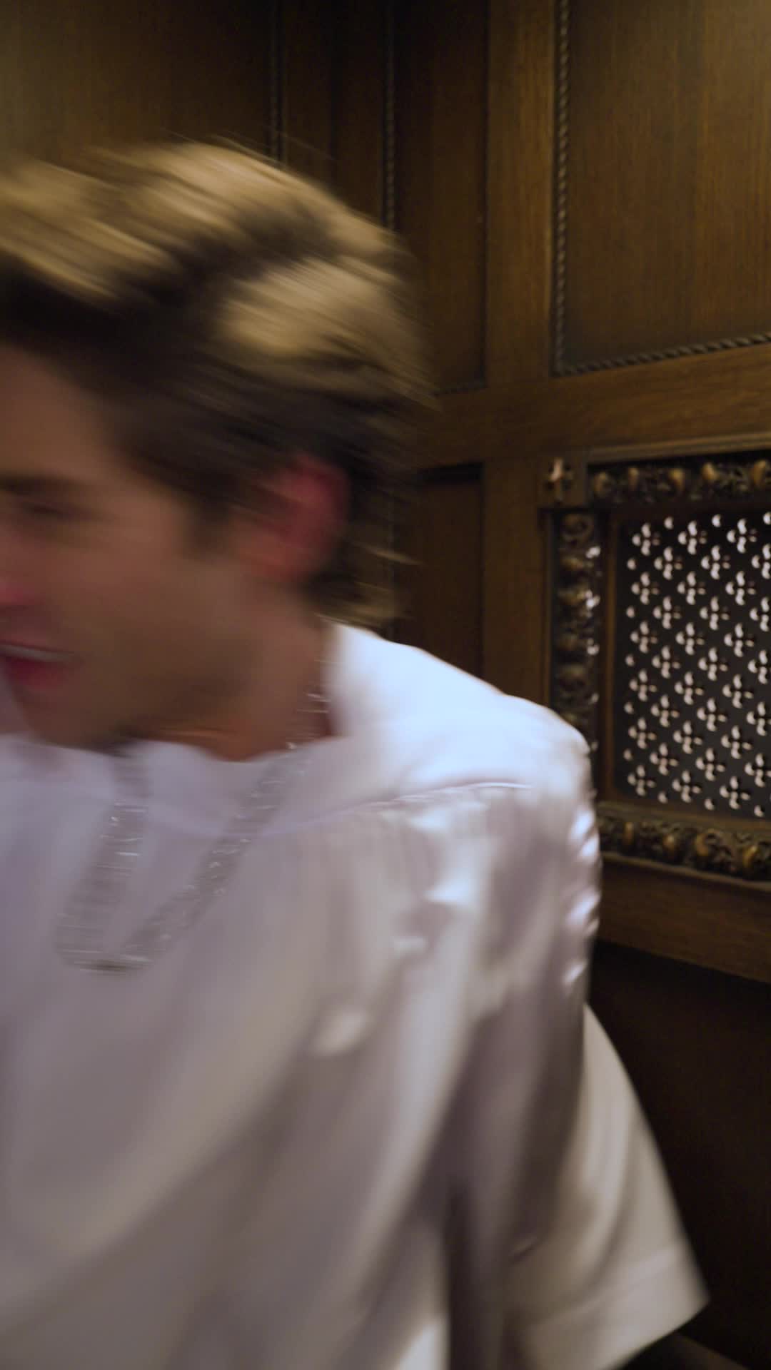 Theo Martin in a white altar-boy robe turning his head inside the wooden confessional, next to the carved screen
