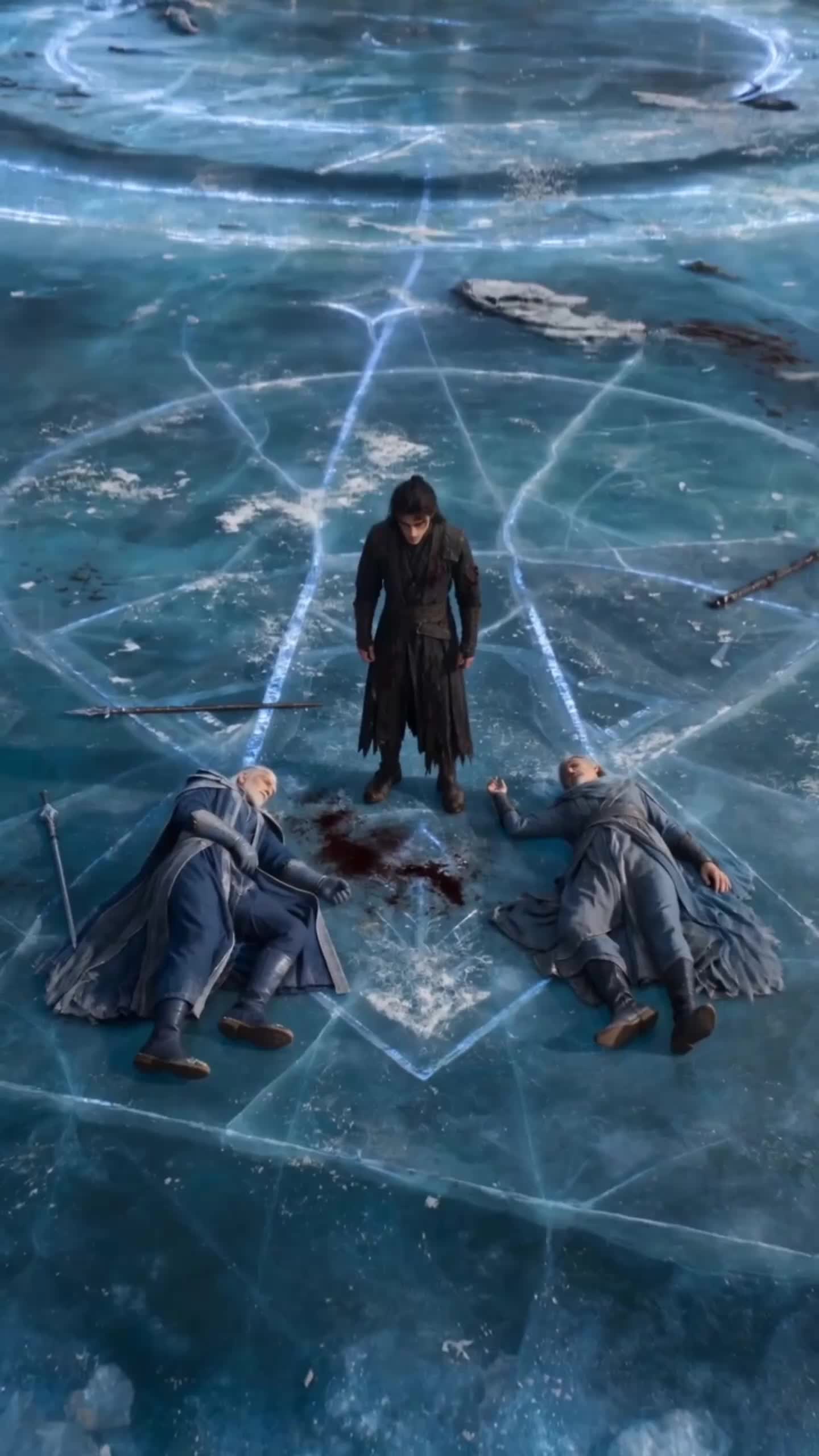 Seen from above, Cedric in black standing on a cracked ice floor traced with glowing blue lines, between two mages in blue robes lying on their backs with their staffs dropped