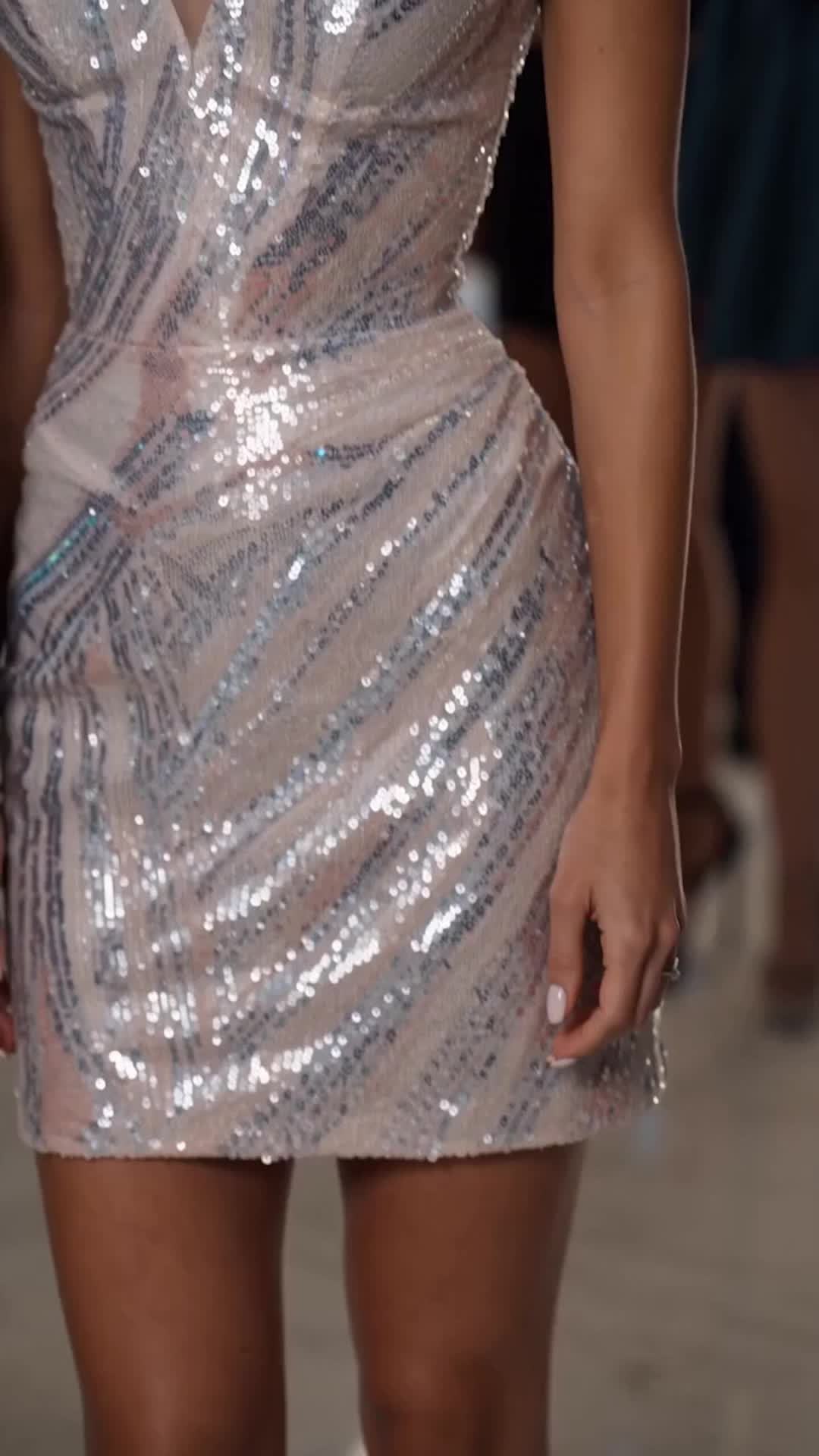 Close-up of a silver sequined mini dress on a woman standing on a pale floor, her hand with white nails at her side